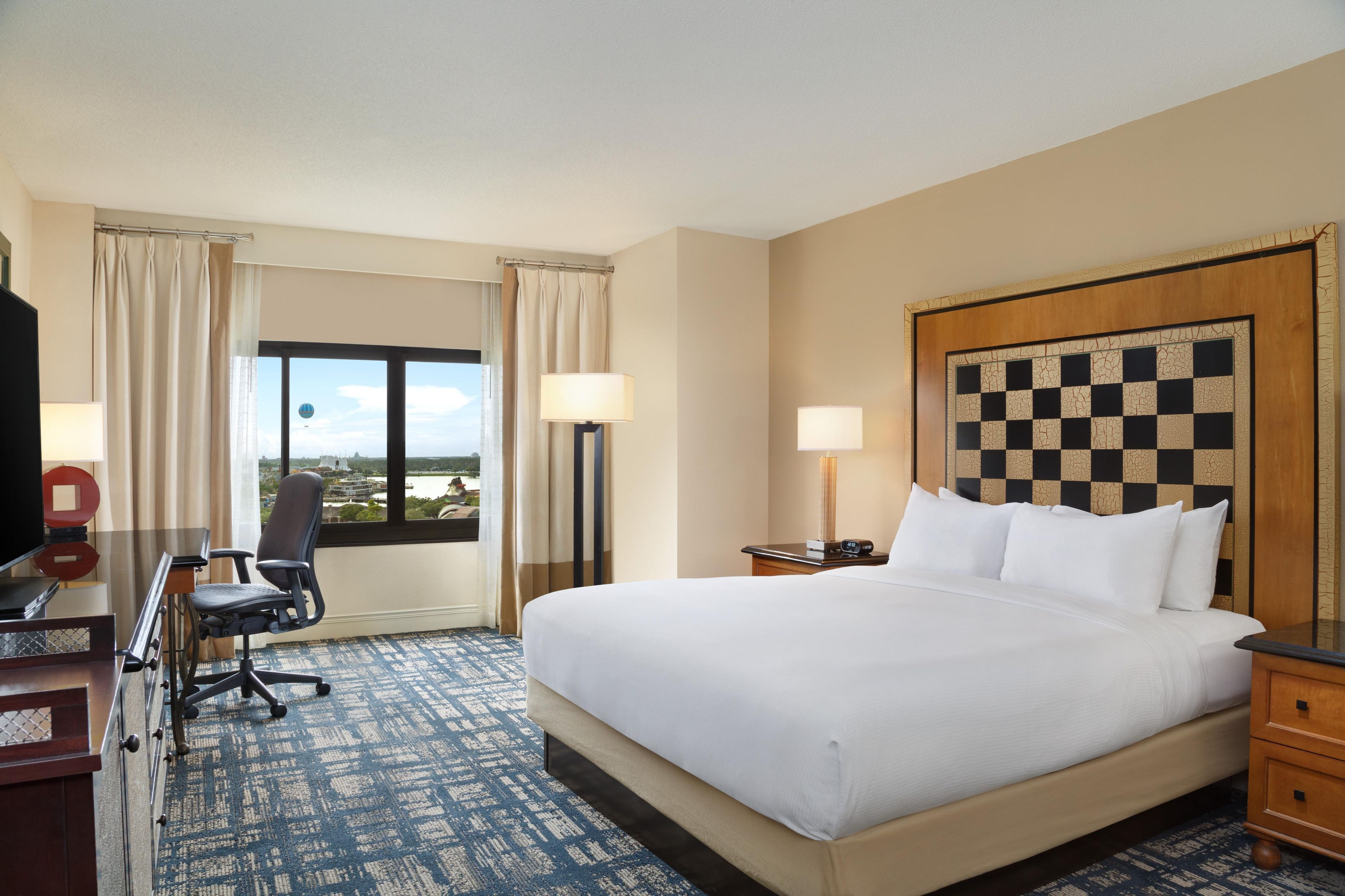 A hotel room with a large bed, a desk with a chair, a TV, and a view of the outdoors.