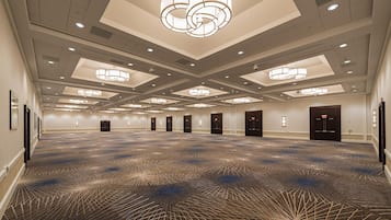 A spacious hotel lobby with a patterned carpet, multiple doors, and a modern chandelier.