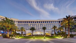 A modern hotel with a central courtyard, palm trees, and a well-lit entrance. - Hilton Orlando Lake Buena Vista - Disney Springs® Area (Lake Buena Vista)
