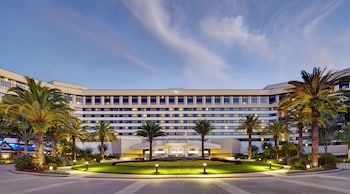 A hotel room with a large bed, a desk, a chair, a small table, and a view of the cityscape. at Hilton Orlando Lake Buena Vista - Disney Springs® Area