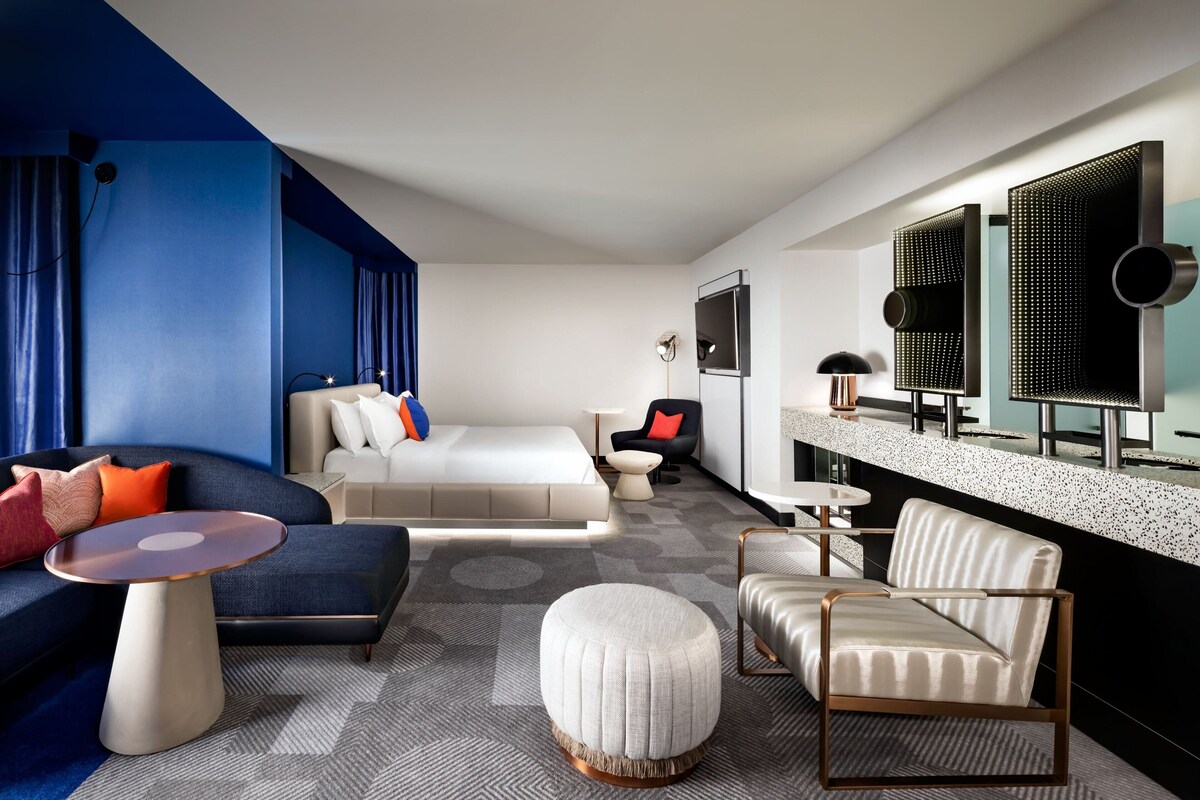 Una habitación de hotel moderna con una cama, un sofá, una mesita de café, una silla y una pequeña mesa.