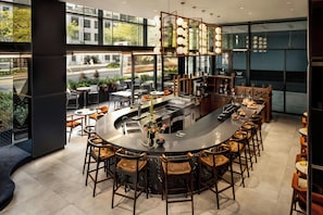 A modern bar area with a curved counter, bar stools, and a view of the street through large windows. - W Toronto (Toronto)