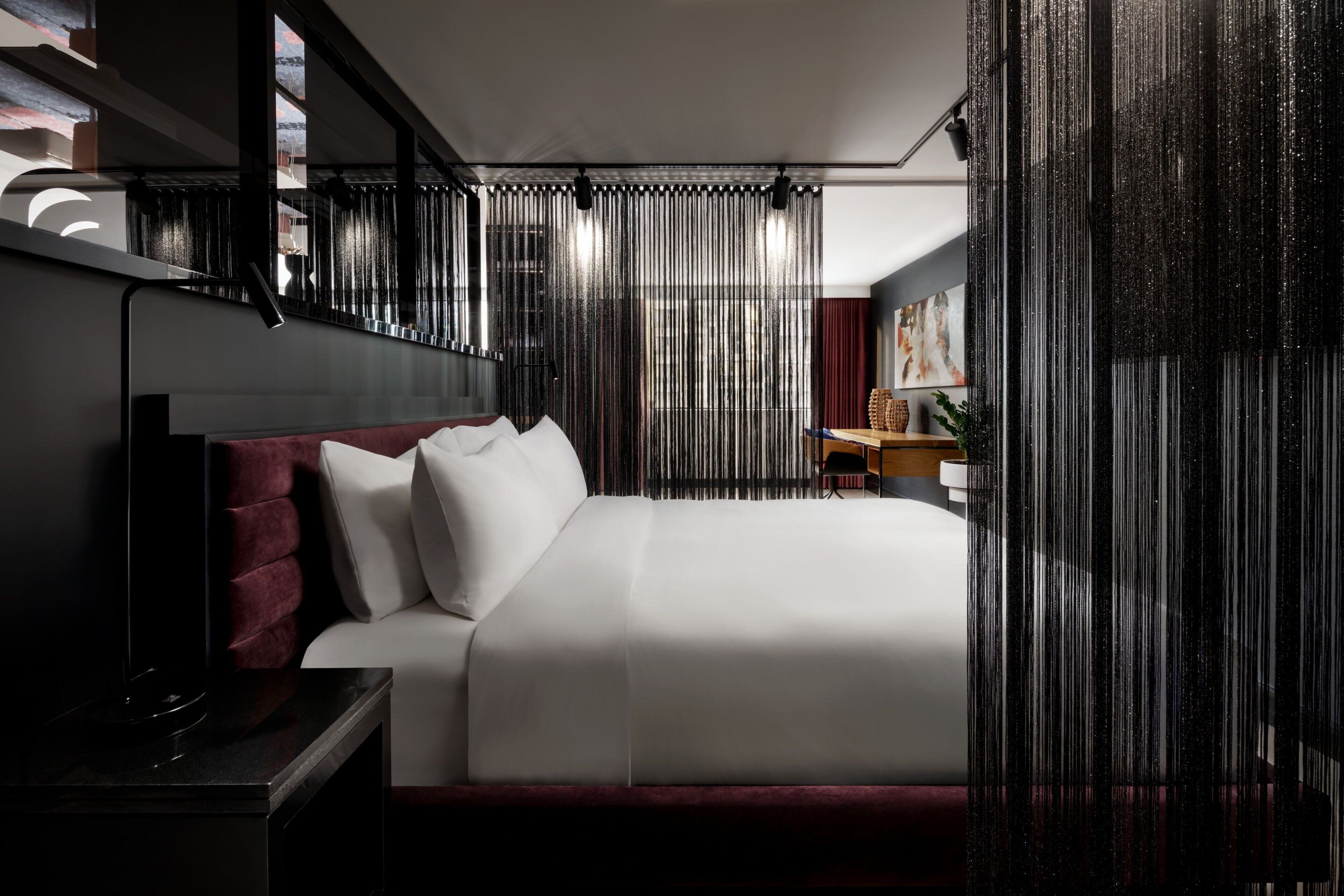 Een moderne hotelkamer met een groot bed, een donker hoofdeinde en uitzicht op de stad door dunne gordijnen.