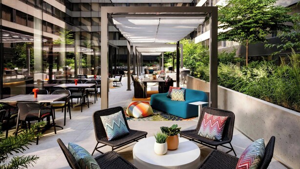 A modern outdoor seating area with tables and chairs, a blue sofa, and potted plants. - W Toronto (Toronto)