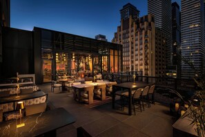 An outdoor dining area with tables and chairs, a bar with a glass enclosure, and a view of tall buildings in the background. - W Toronto (Toronto)
