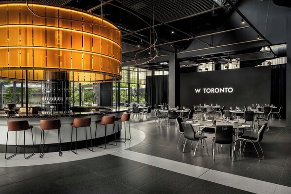 A modern bar area with a circular light fixture, bar stools, and a projection screen displaying 'W TORONTO'.