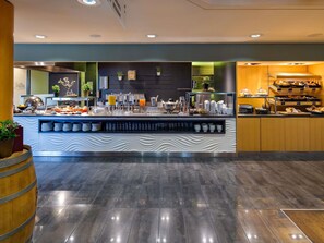Una barra de desayuno moderna con diversas opciones de comida y bebida, como frutas, jugos y pastelería.