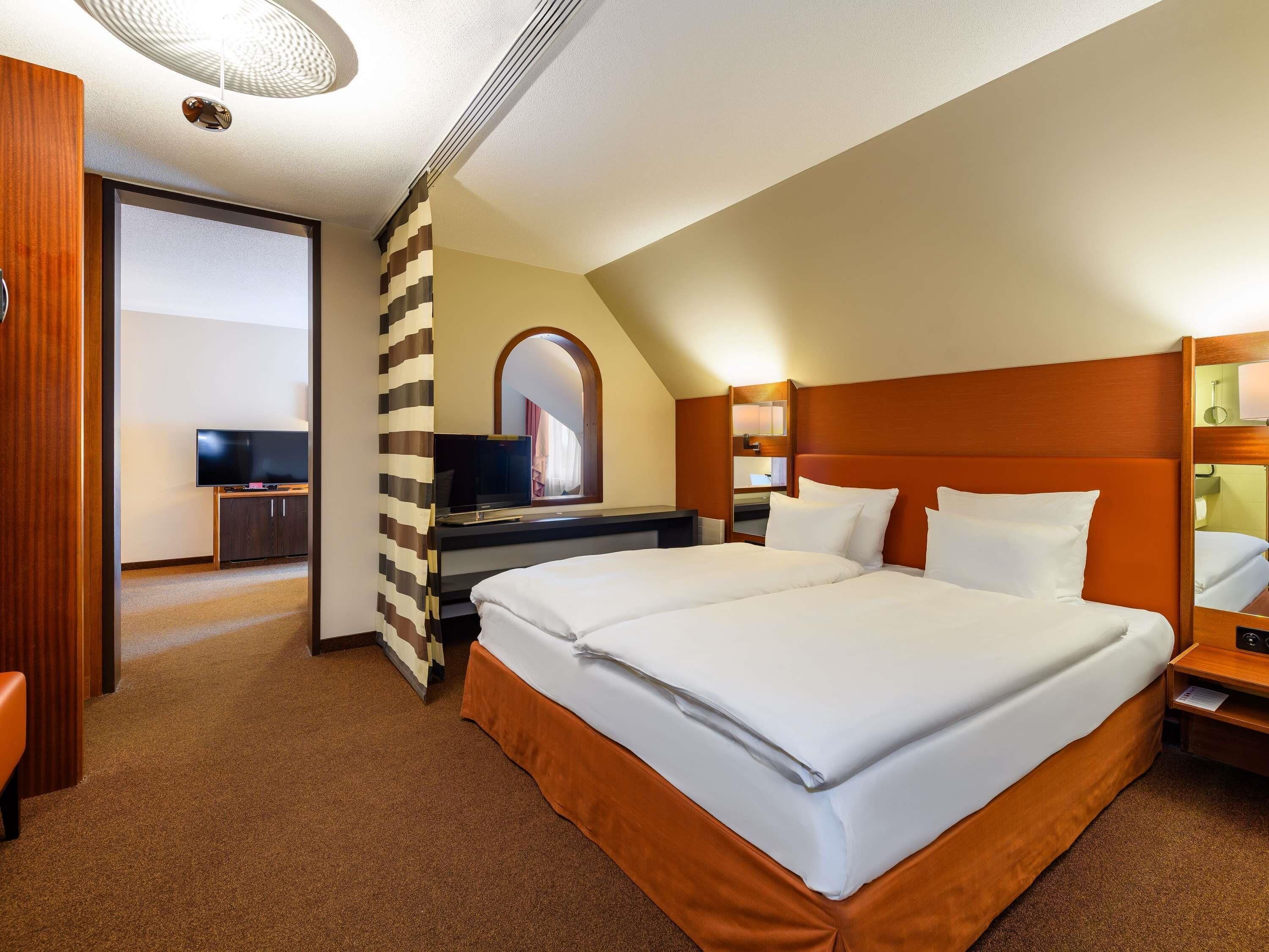 Una habitación de hotel con una cama grande, un escritorio con televisor y un espejo sobre la cama.