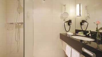 A modern bathroom with a glass shower enclosure, a black countertop vanity, a large mirror, and a single white towel.