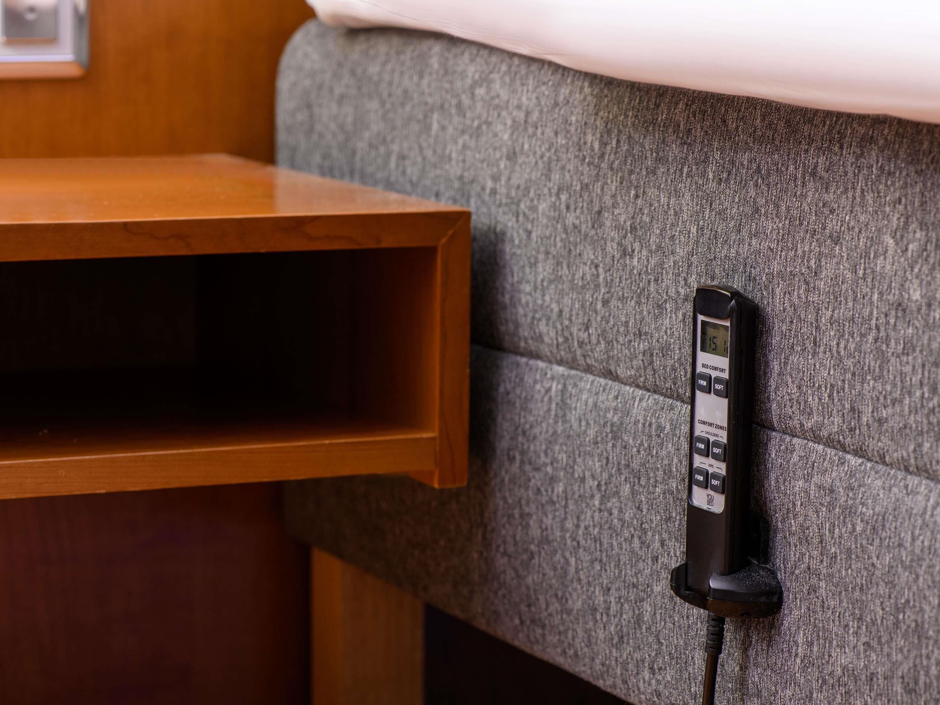 A control panel on a grey upholstered headboard with a wooden side table.