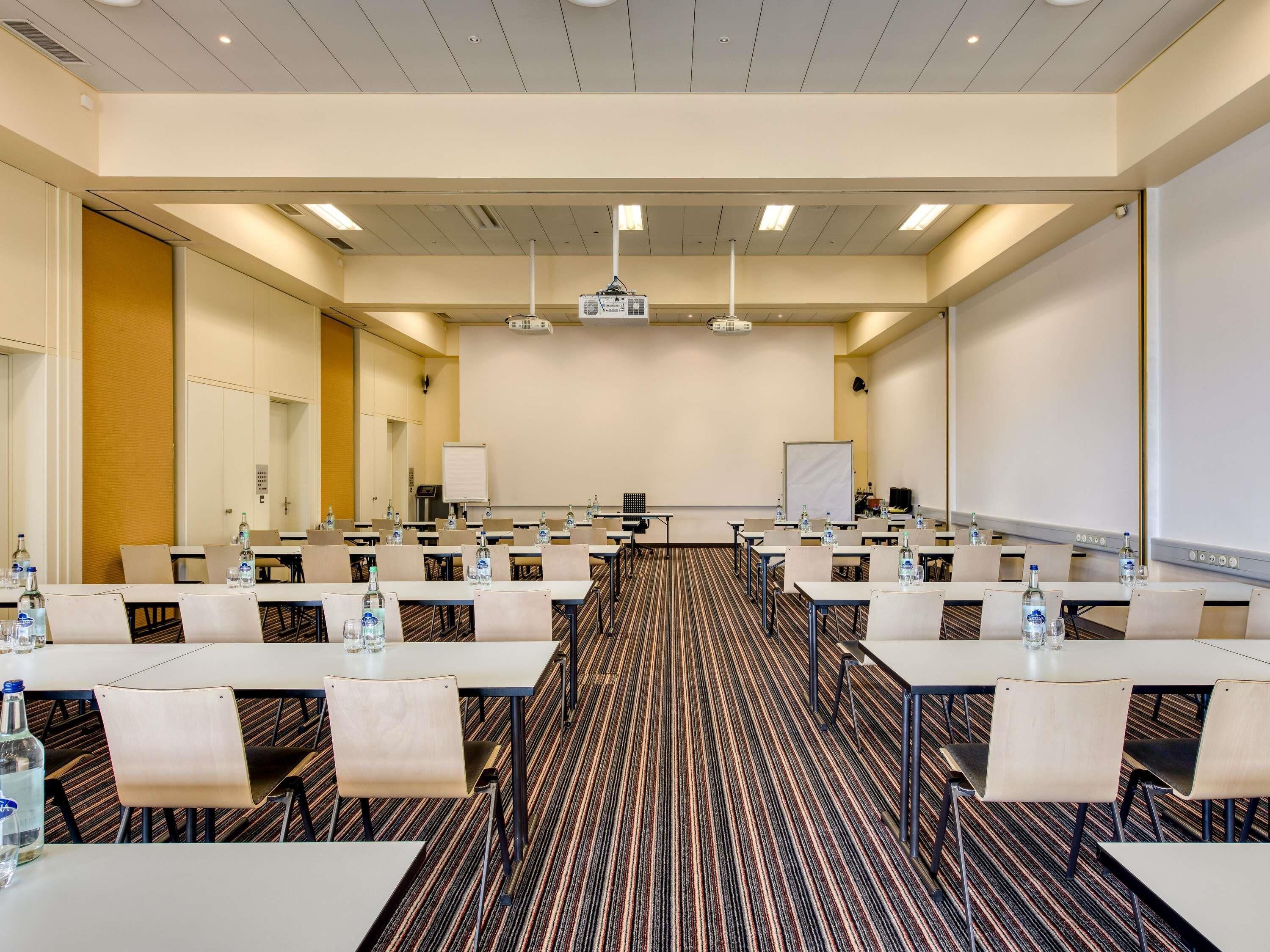 Un salón de conferencias con varias mesas, sillas, un proyector y una pizarra.