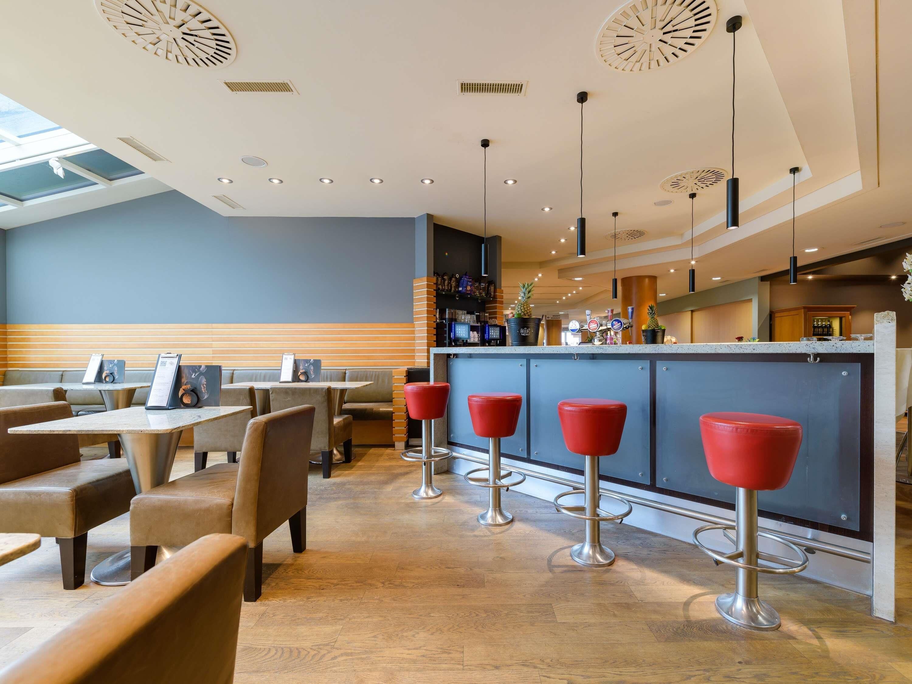 A modern restaurant interior with high ceilings, recessed lighting, and a bar area with stools.