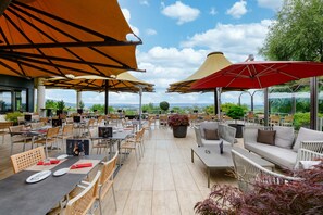 Un espacio de comedor al aire libre con mesas y sillas, grandes sombrillas y vistas del paisaje.