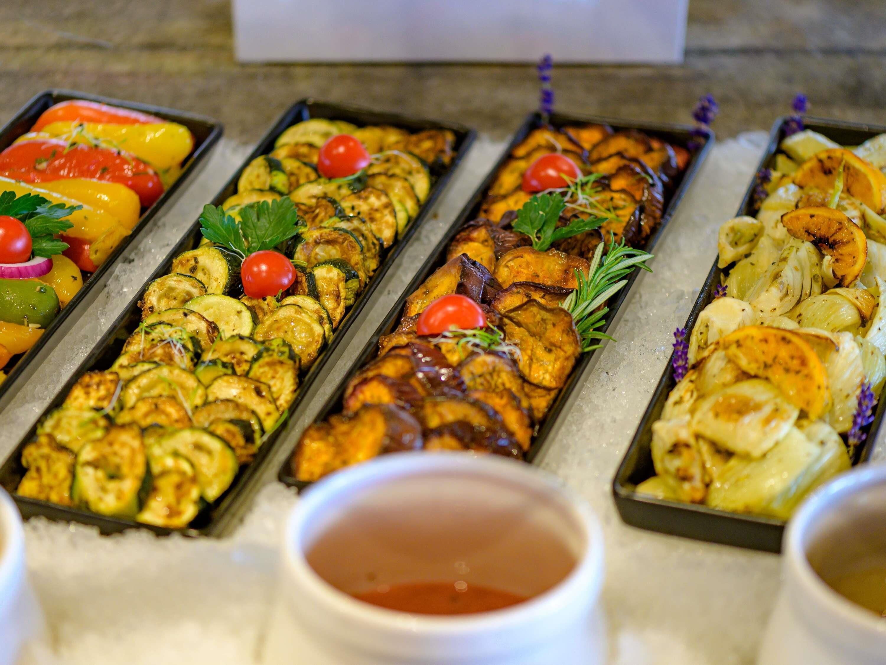 A buffet with various grilled vegetables and a small bowl of sauce in the foreground.