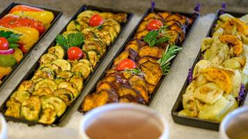 A buffet with various grilled vegetables and a small bowl of sauce in the foreground.