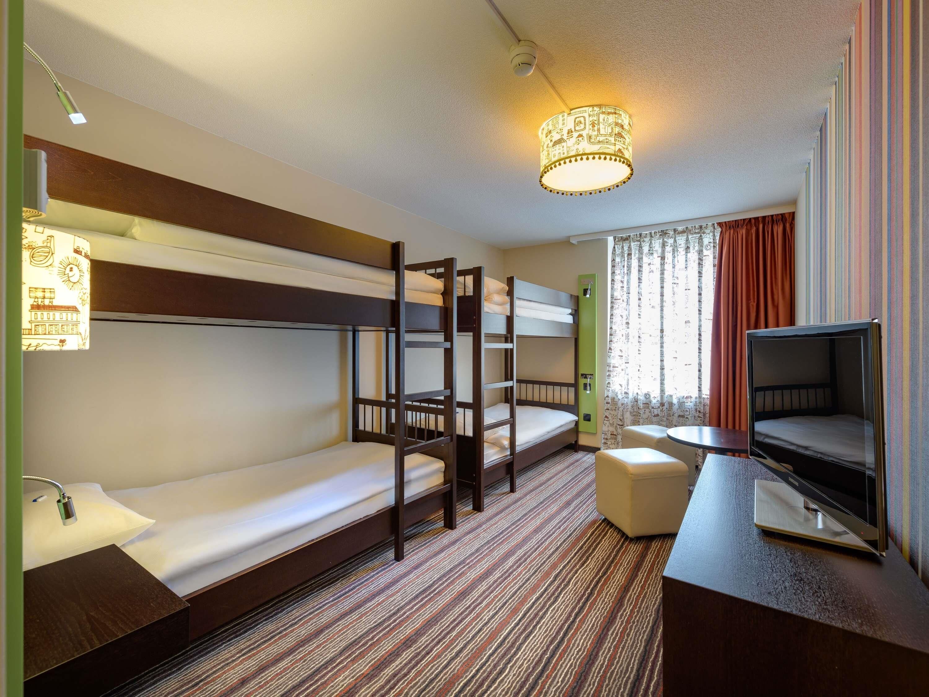 Habitación de hotel con literas, televisor, escritorio y alfombra estampada.