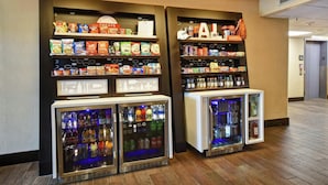 Un vestíbulo de hotel con estantes de aperitivos, dispensadores de bebidas y una zona de recepción.