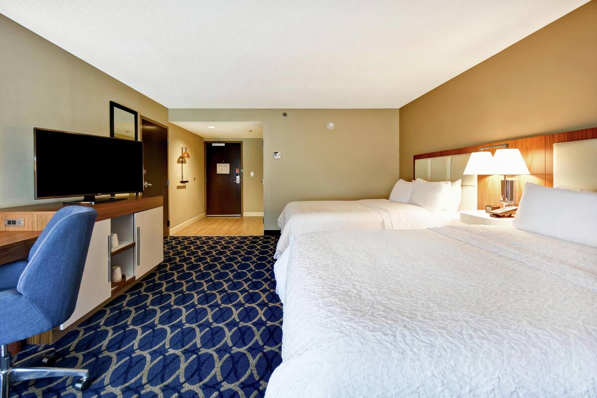 A hotel room with a bed, a desk with a chair, a television, and a lamp.