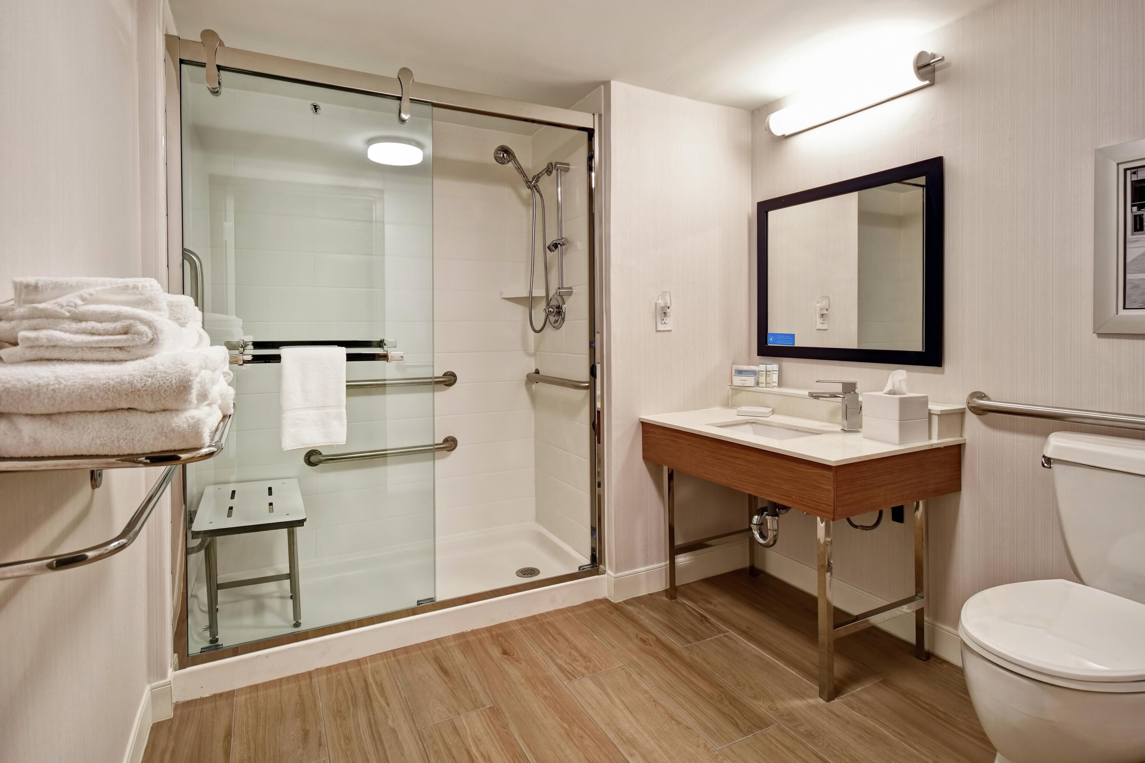 A modern bathroom with a glass-enclosed shower, a wooden vanity, and a white toilet.