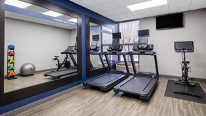 Un gimnasio con cintas de correr, pelotas de ejercicio y un espejo grande.