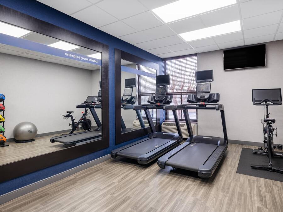 Une salle de sport équipée de tapis de course, de ballons d’exercice et d’un murmiroir.