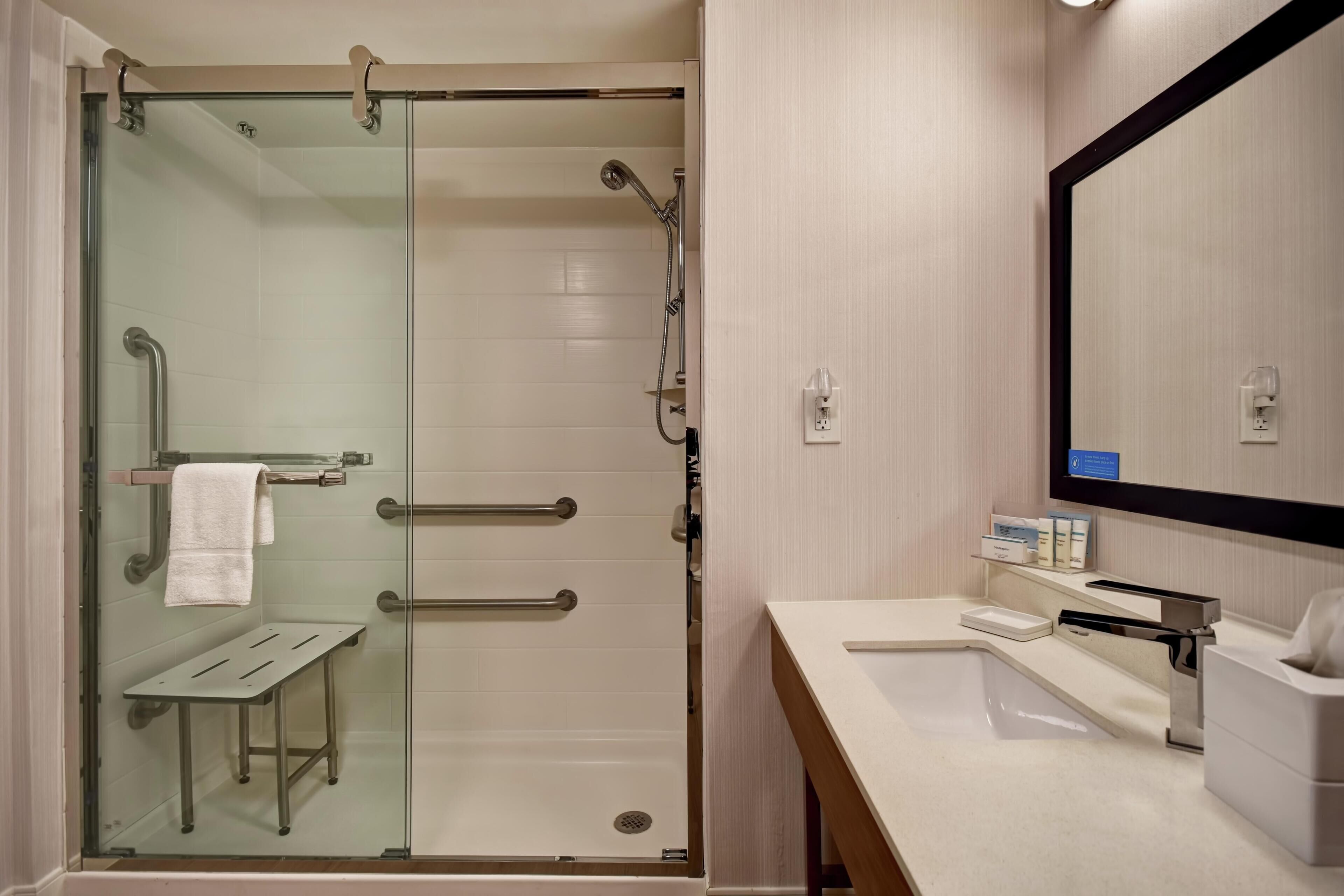 A modern bathroom with a glass-enclosed shower, a sink, a mirror, and a towel rack.
