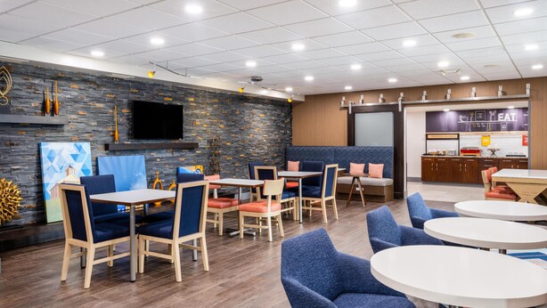 Un restaurante moderno con suelo de madera, sillas tapizadas en azul y una zona de cocina con un letrero que dice 'EAT'.