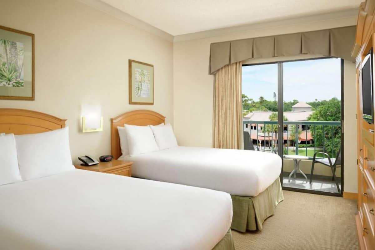 Une chambre d’hôtel avec deux lits, un balcon avec vue et une télévision.