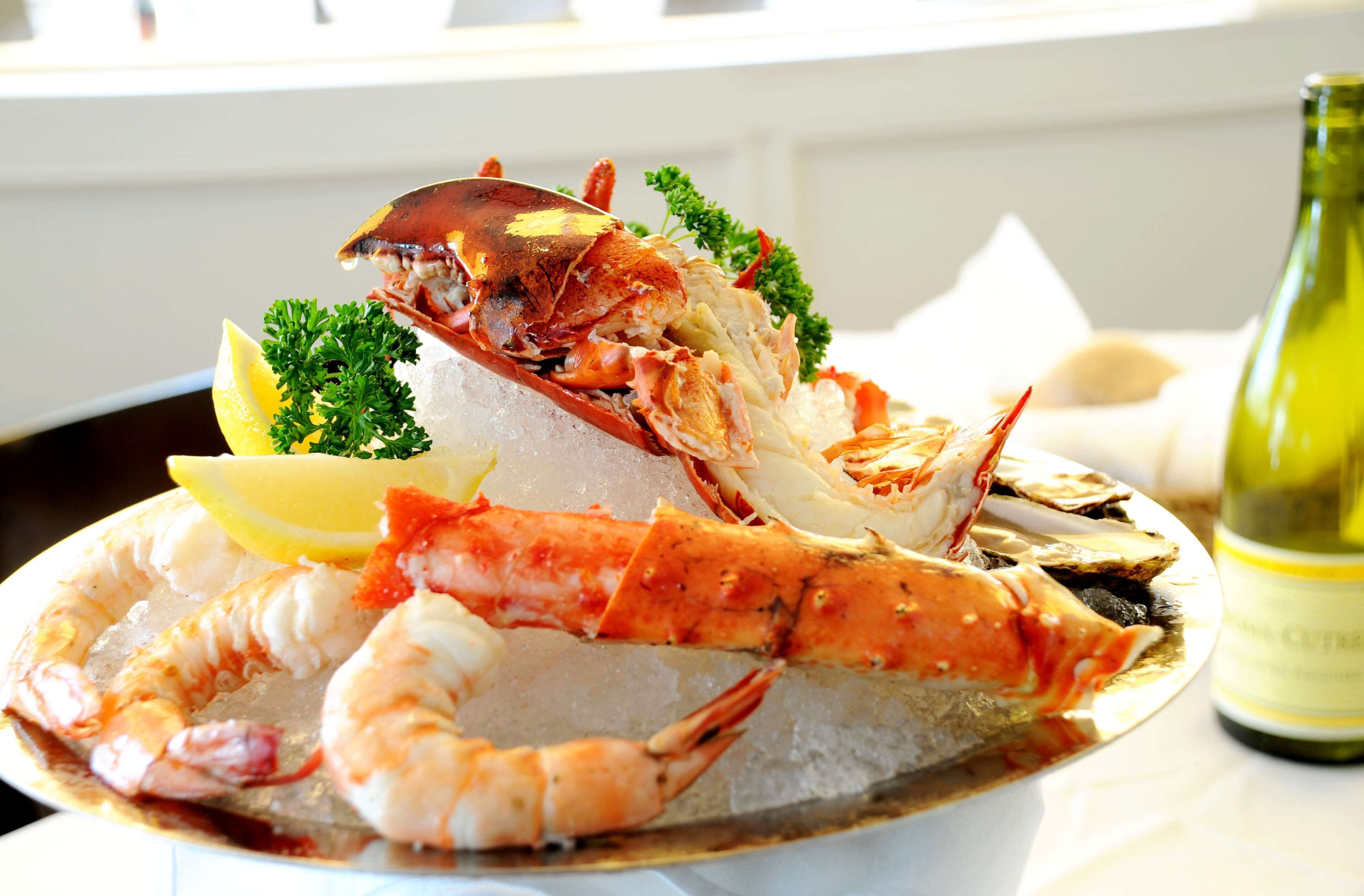 A seafood platter with lobster and shrimp on ice, garnished with parsley and lemon, with a bottle of white wine in the background.