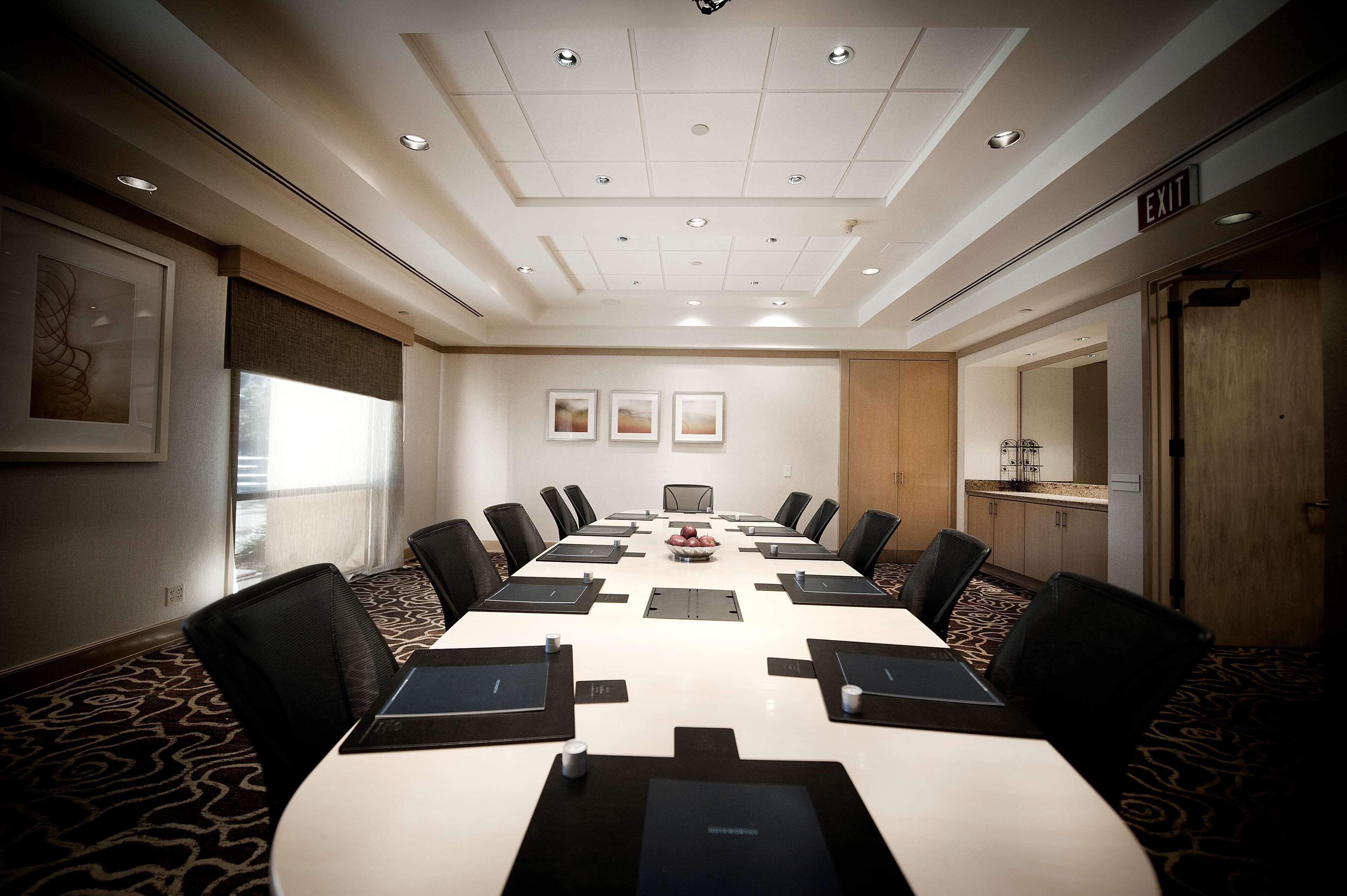 Un salón de conferencias con una larga mesa, sillas y un techo blanco con iluminación empotrada.