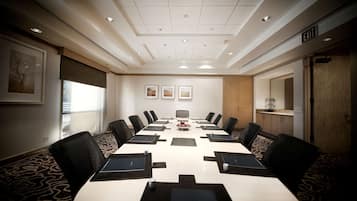 Un salón de conferencias con una larga mesa, sillas y un techo blanco con iluminación empotrada.