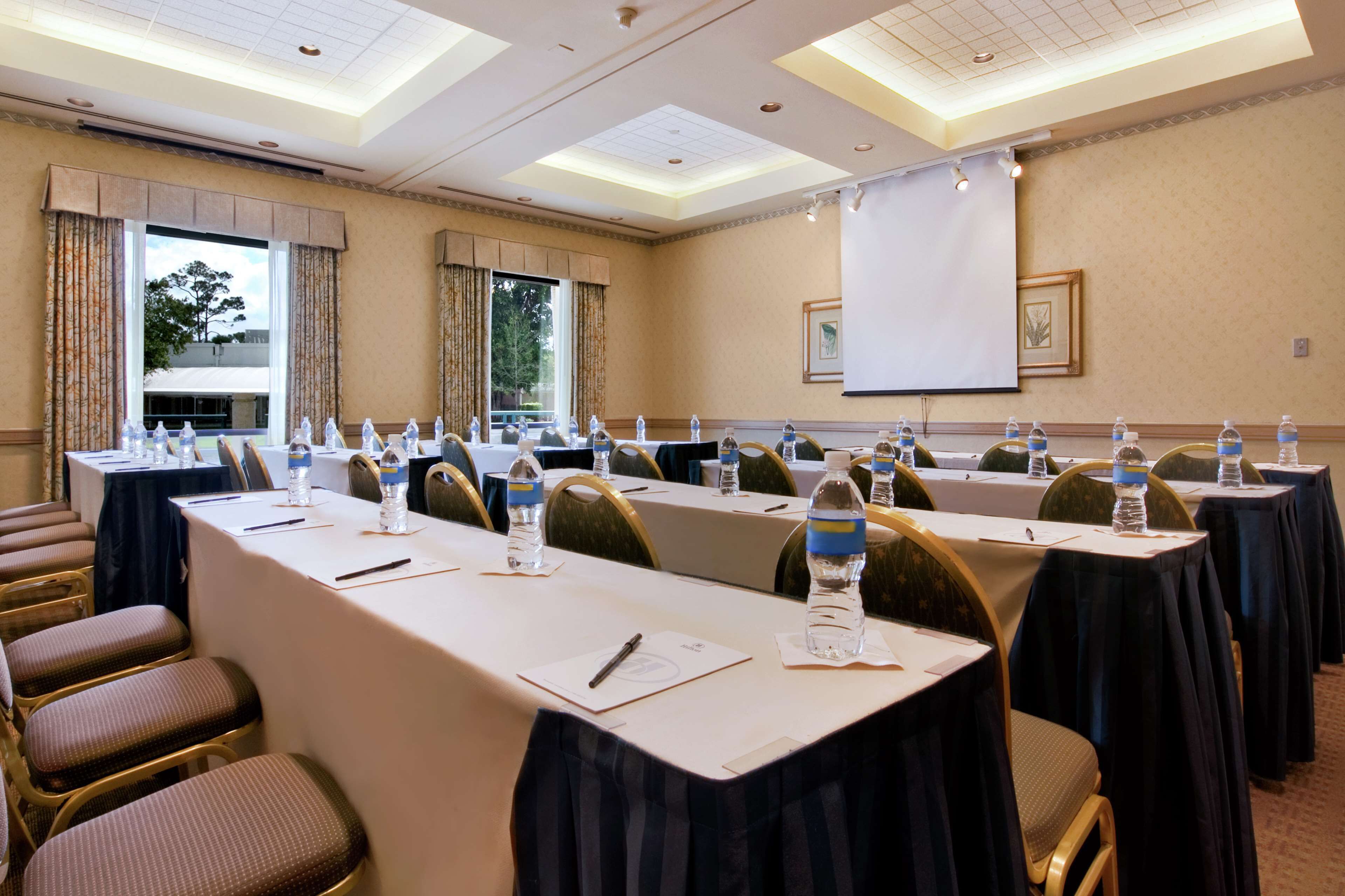 A conference room with long tables, chairs, water bottles, and a projector screen.