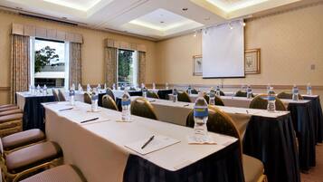A conference room with long tables, chairs, water bottles, and a projector screen.
