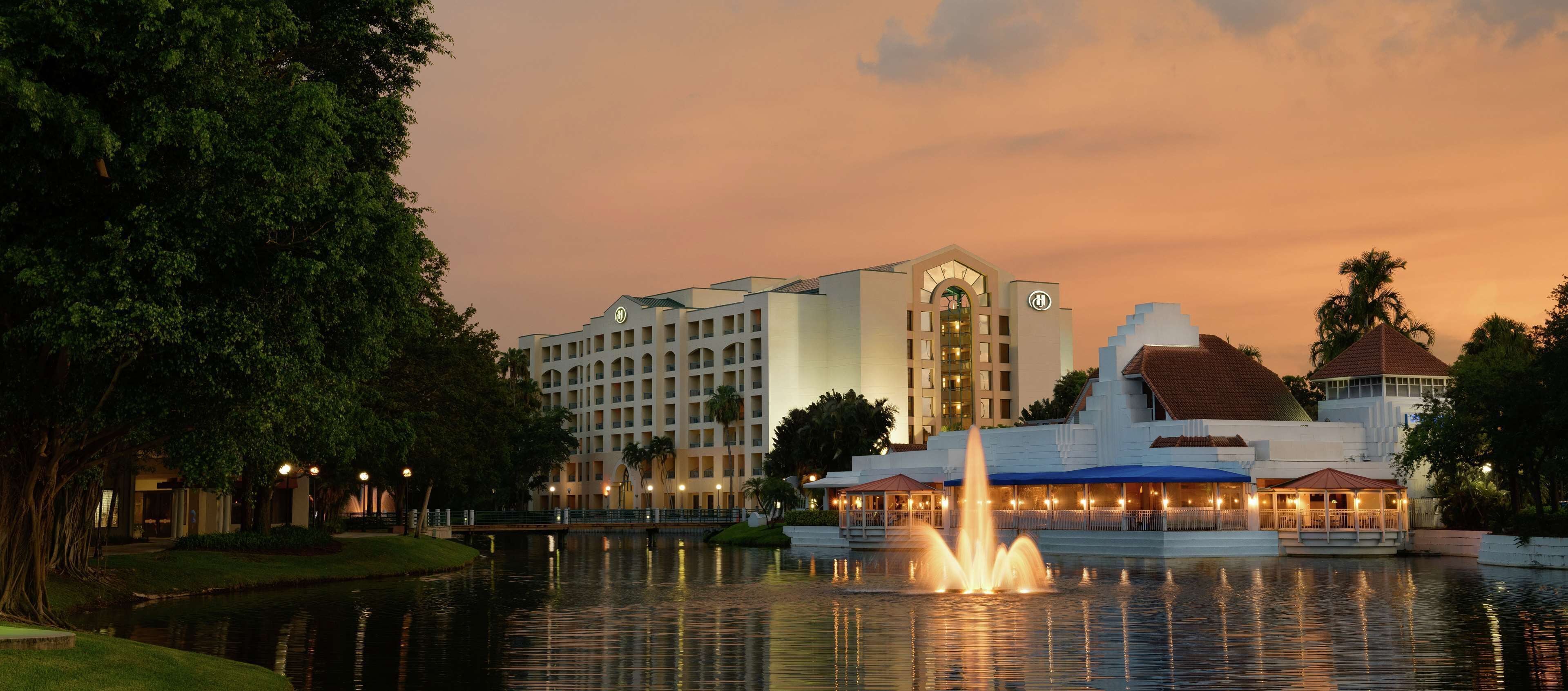 A hotel with a large building, a fountain, and a body of water.