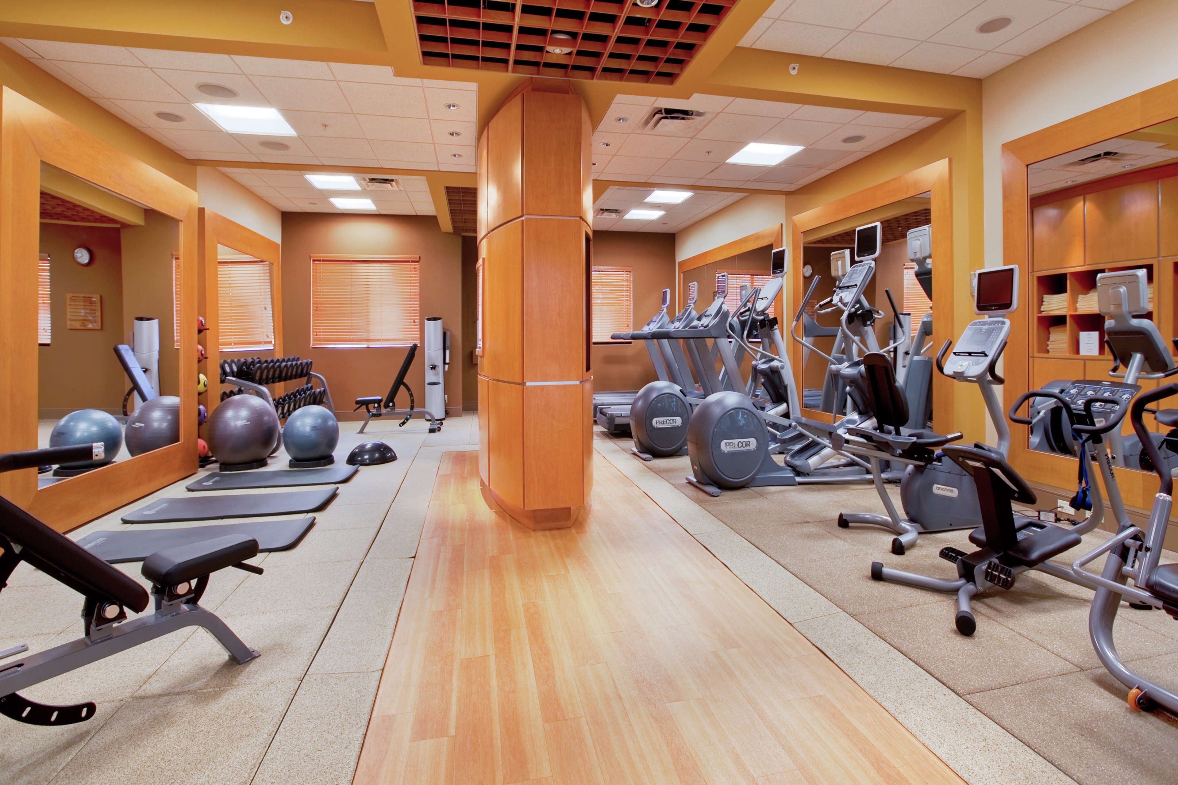 A gym with exercise equipment, mirrors, and wooden flooring.