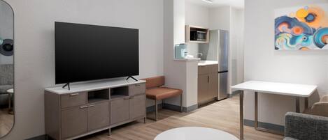 A modern living room with a flat-screen TV, a sofa, a coffee table, and a kitchen area in the background.