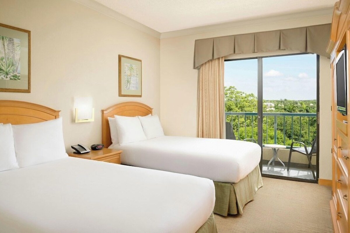 A hotel room with two beds, a balcony with a view, a TV, and a telephone on the nightstand.