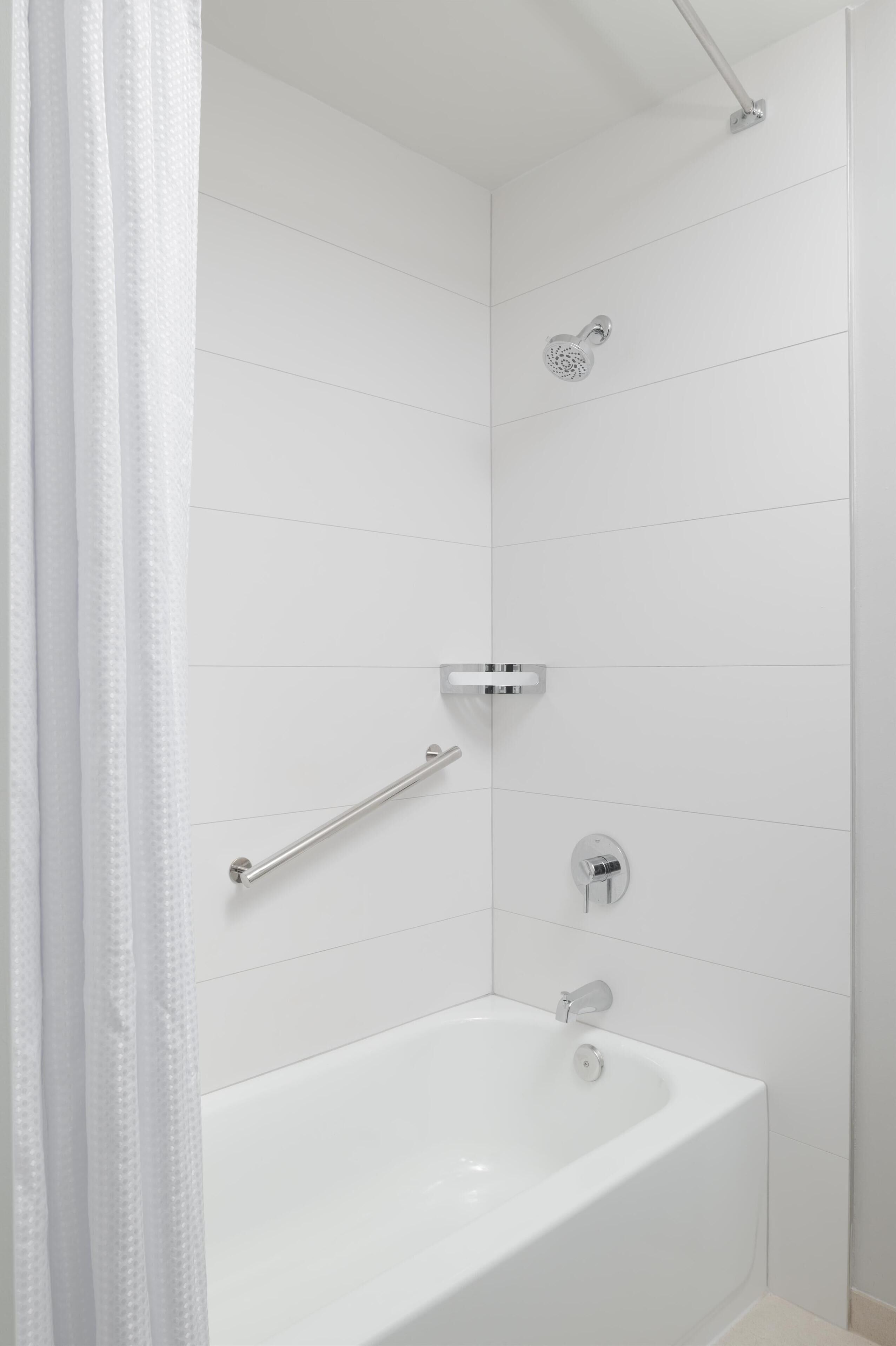 A modern bathroom with a white bathtub, a handheld showerhead, a grab bar, and a towel rack.