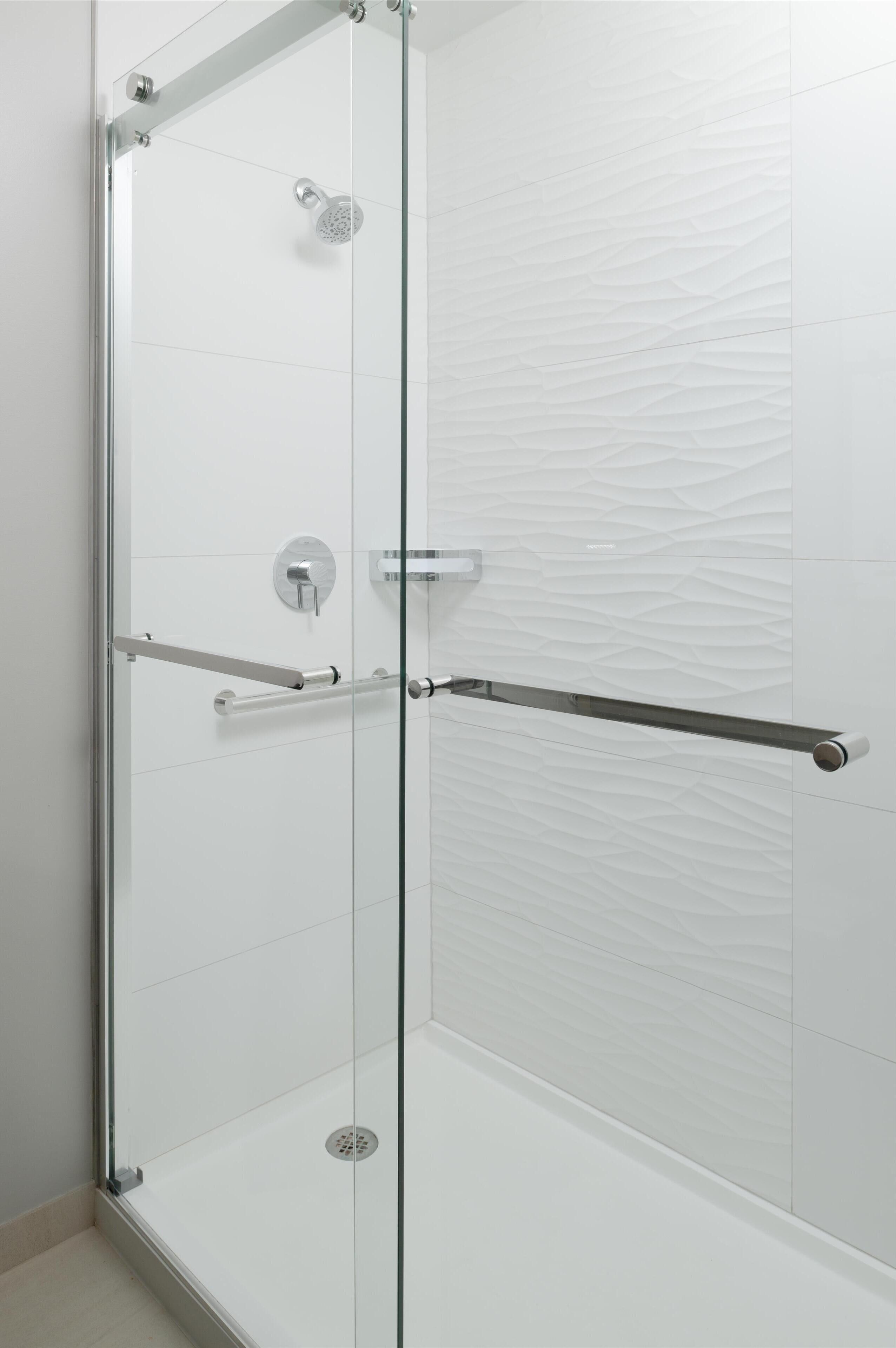 A glass-enclosed shower with a handheld showerhead and a handheld bar.