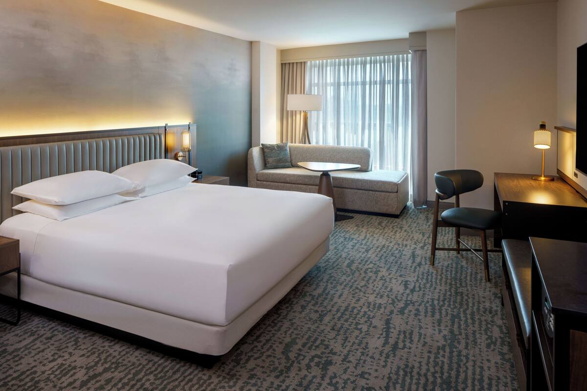 Ein Hotelzimmer mit einem großen Bett, einem Schreibtisch, einem Stuhl, einer kleinen Couch und einem Fernseher.