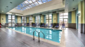 An indoor swimming pool with clear glass ceiling, blue lounge chairs, and a fire extinguisher.
