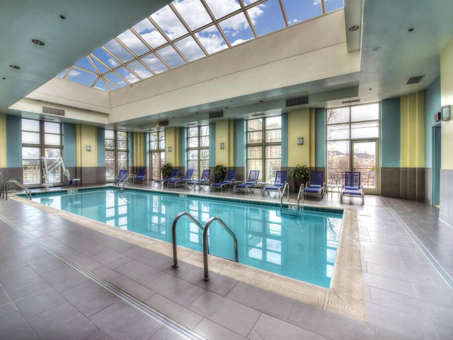 An indoor swimming pool with clear glass ceiling, blue lounge chairs, and a fire extinguisher.