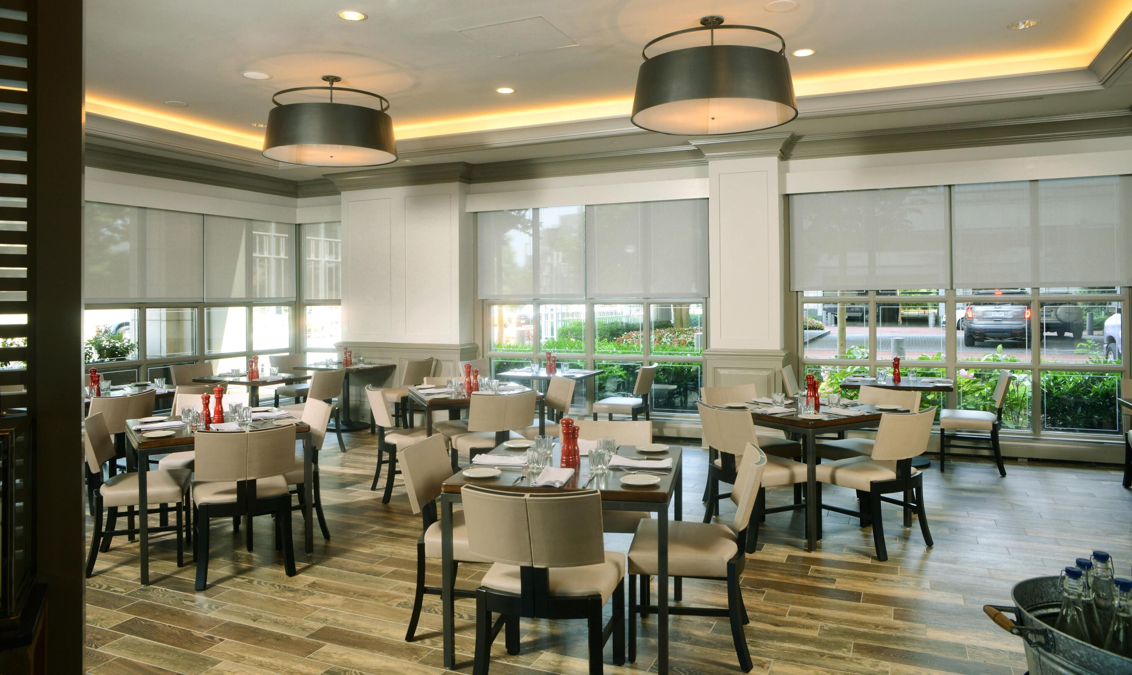 A restaurant with multiple tables and chairs, large windows, and a modern ceiling design.