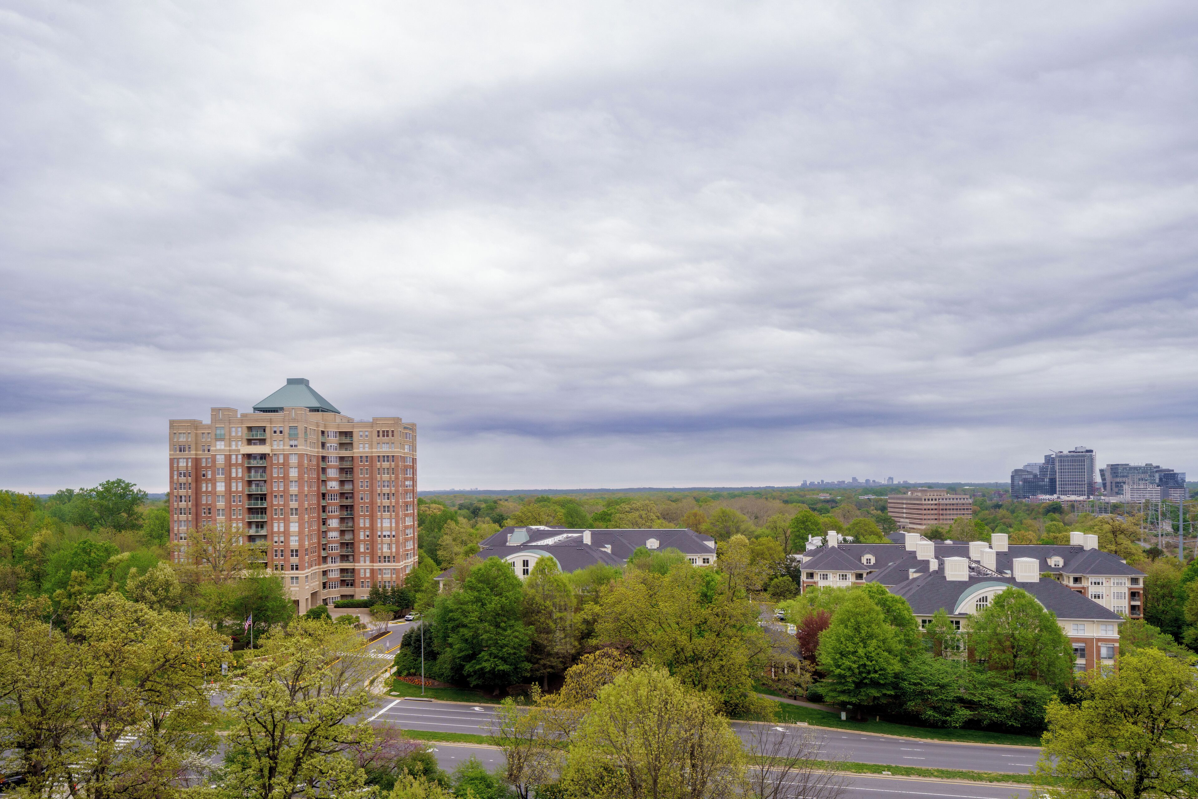 A high-rise building with a distinctive green roof, surrounded by lush greenery and a road.