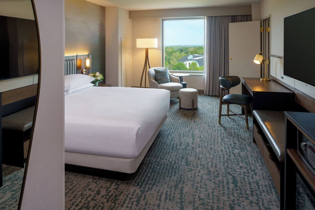 Ein Hotelzimmer mit einem großen Bett, einem Schreibtisch, einem Stuhl, einem kleinen Tisch und einem Fernseher.