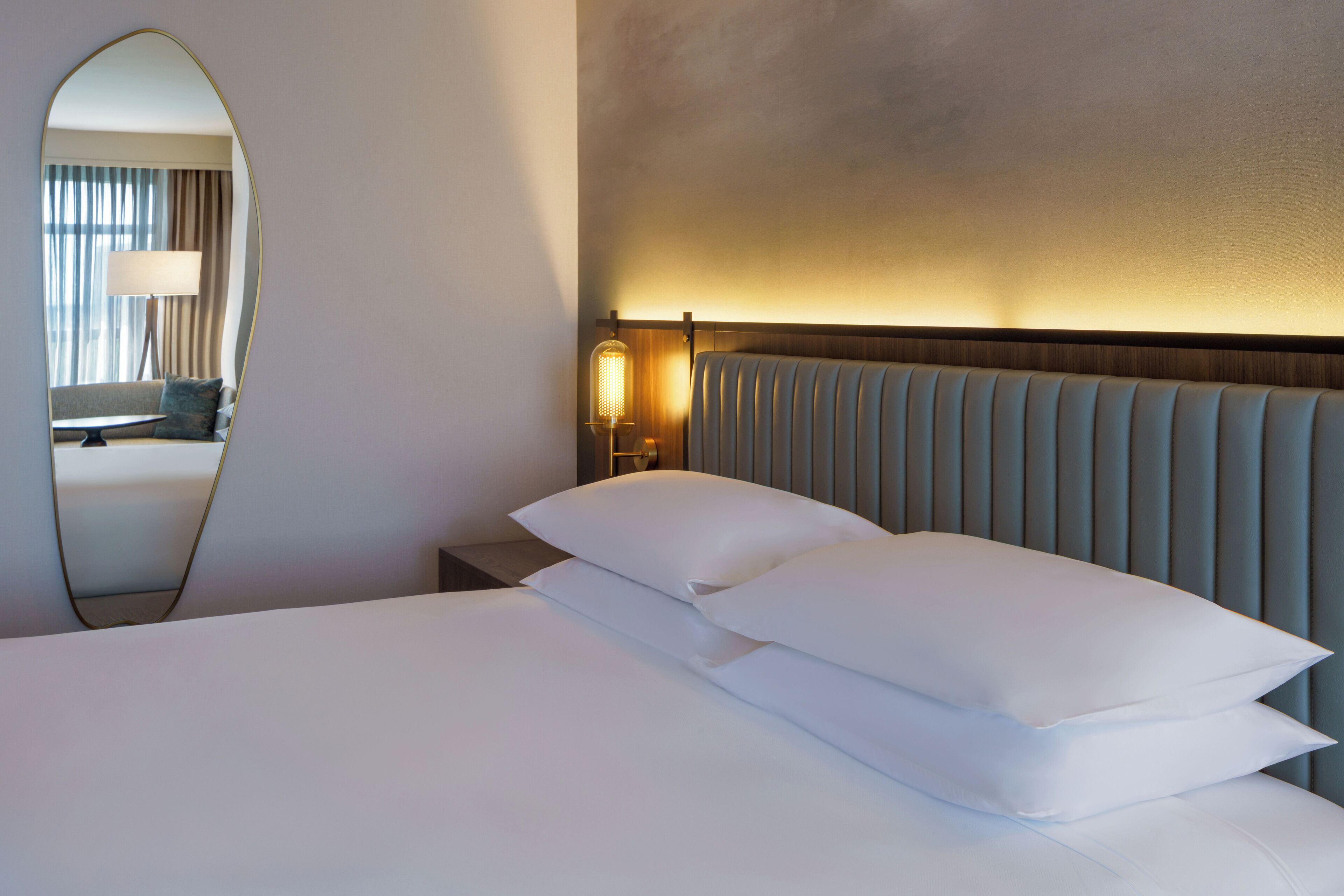 Een hotelkamer met een groot bed, nachtkastje, lamp en spiegel.