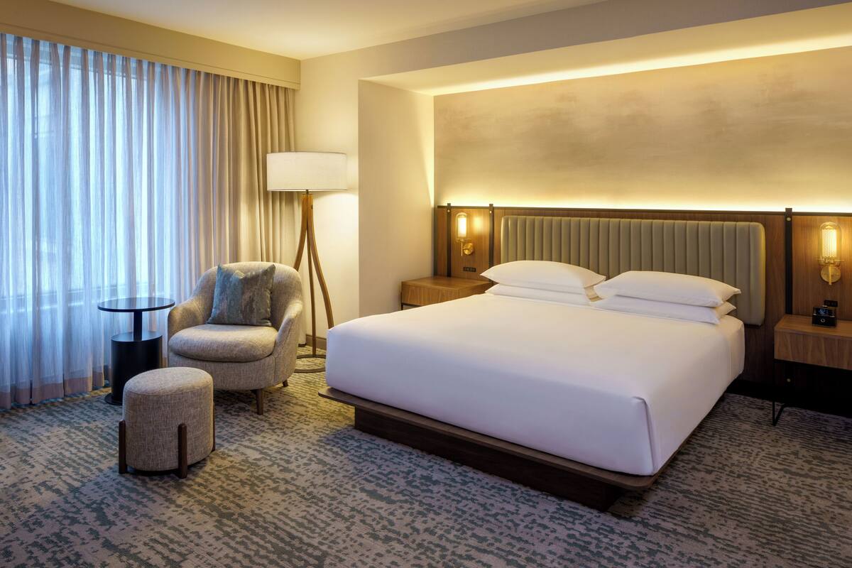 Ein Hotelzimmer mit einem großen Bett, einem Sessel, einem kleinen Tisch und einer Lampe.