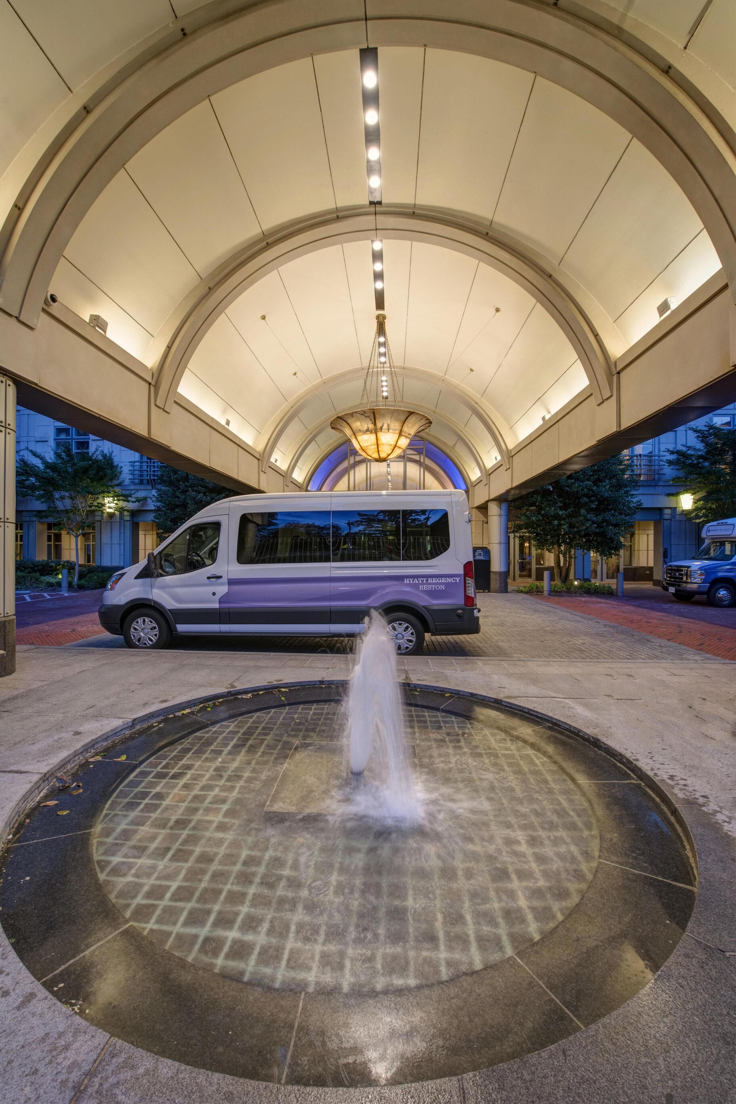 A hotel entrance with a fountain, a van, and a covered walkway.
