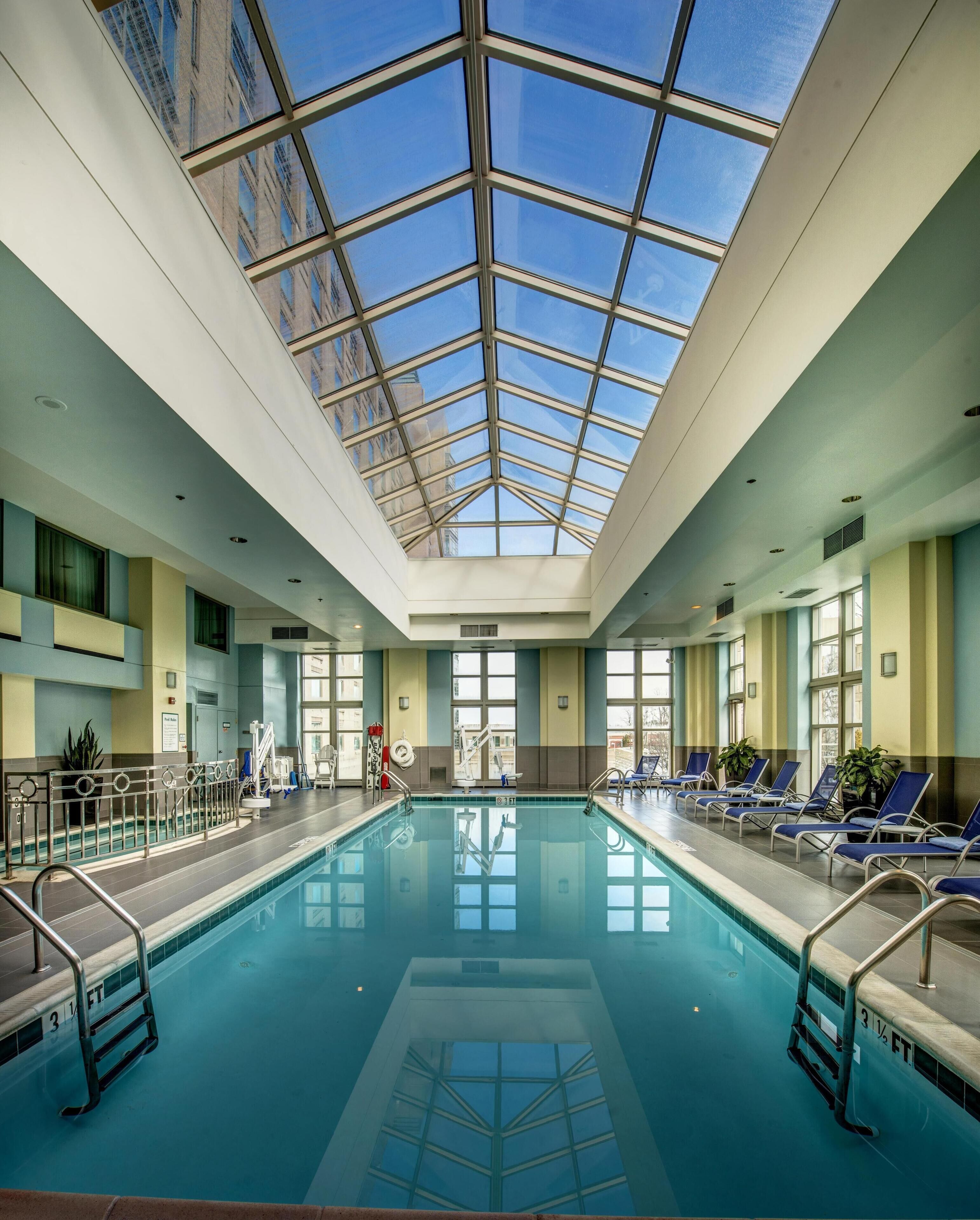 Une piscine intérieure dotée d’un toit en verre, de chaises disposées au bord du bassin et d’un poste de surveillance pour les sauveteurs.