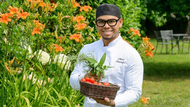 A chef holding a basket of fresh produce and herbs.